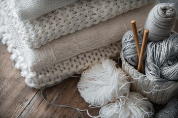 A woven basket with white and gray thread for knitting and knitting needles. White sweaters and...