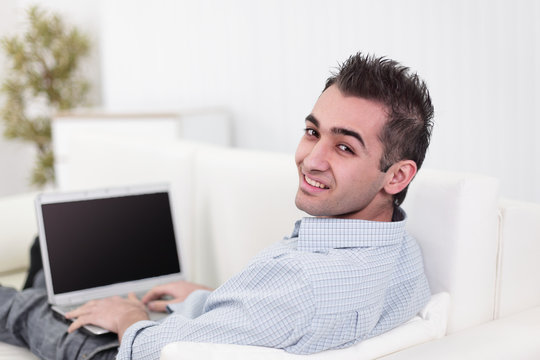 Handsome man is using a laptop, looking at camera and smiling
