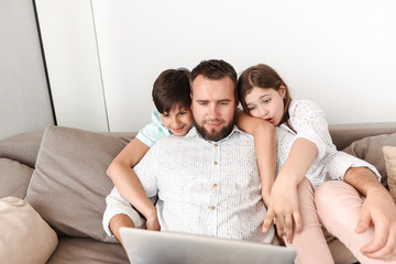 Picture of lovely family father 30s with son and daughter 8-10 sitting together on couch at home, and using silver laptop