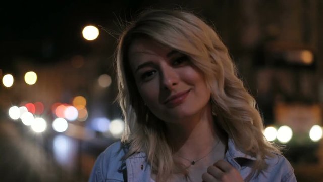 Portrait of beautiful young blonde woman against night shined city. City lights background