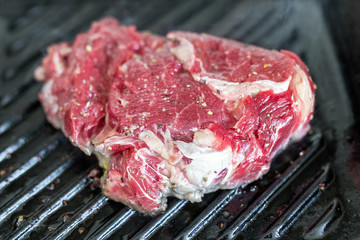 Close-up raw tasty fresh rib eye steak on grill cast iron pan. Organic beef meat seasoned with ground pepper coocked on barbeque