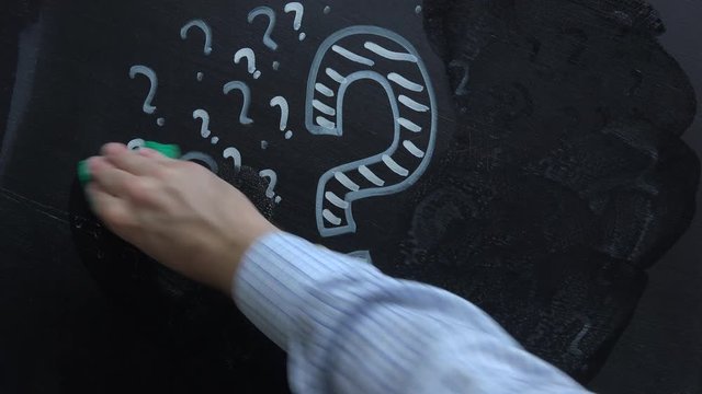 Hand erasing question marks from blackboard, concept of perplex and confusion