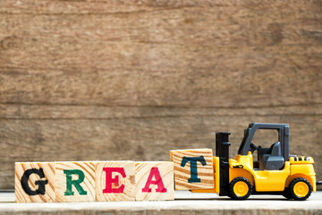 Yellow plastic toy forklift hold letter block T to complete word great on wood background