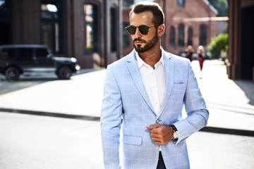 Portrait of sexy handsome fashion businessman model dressed in elegant blue suit posing on street background. Metrosexual