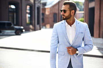 Portrait of sexy handsome fashion businessman model dressed in elegant blue suit posing on street background. Metrosexual