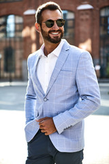 Portrait of sexy handsome fashion businessman model dressed in elegant blue suit posing on street background. Metrosexual