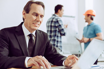 Progressive man. Elegant calm cheerful worker looking at the screen of a laptop while his...