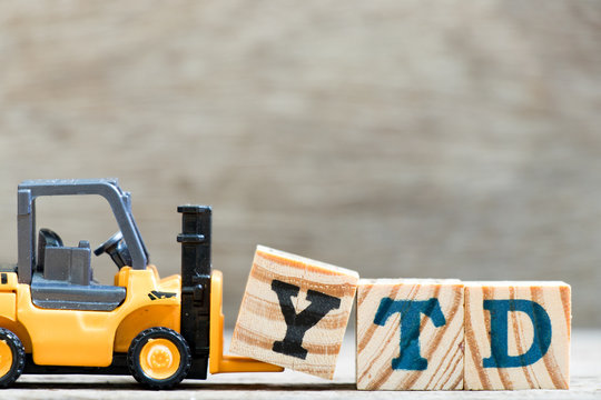 Toy forklift hold letter block Y in word YTD (abbreviation of year to date) on wood background