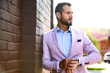 Portrait of sexy handsome fashion businessman model dressed in elegant suit posing near brick wall...