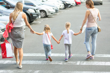 Group of four girl friends walking together through crosswalk . Two young woman with two daughters having fun outdoors near shopping mall. Children and adults friendship concept