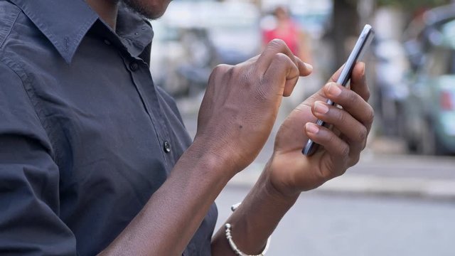 black man's hands scrolling on smartphone in the street- technology,modernity