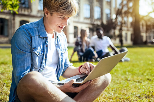 Break on nature. Handsome man keeping smile on his face and bowing head while sitting in semi position in front of his computer