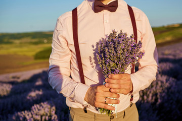 Close-up of a bouquet of lavender in the hands of the groom in the field of lavender.