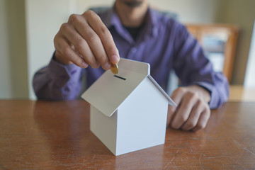Selective focus of young man inserting gold coin into saving box as buying house concept