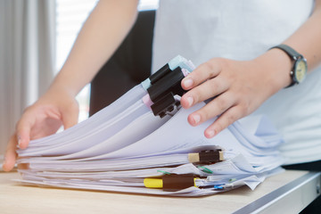 Fototapeta na wymiar Business Documents concept : Employee woman hands working in Stacks paper files for searching and checking unfinished document achieves on folders papers at busy work desk office. Soft focus