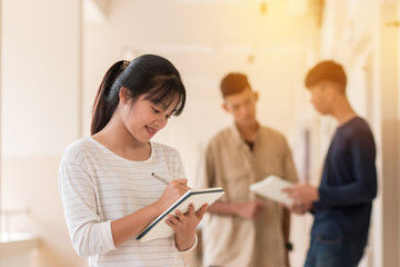 Fototapeta premium Education learning Concept: Confident Asian Students Cute girl taking note with smiling at Outside classroom in university with blur young mens her friends background