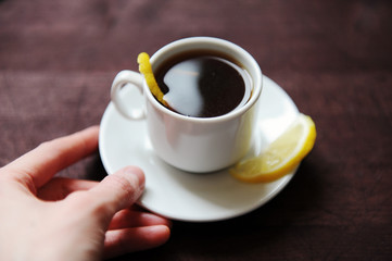 Espresso romano coffee with lemon in a white cup on a dark wooden table. Hold in hand close up