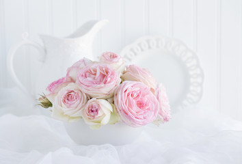 Vintage style still life of a bouquet of pink Eden roses in a white bowl on white