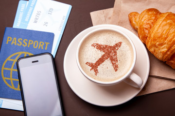 Mug of coffee with an airplane on the foam. Morning coffee with croissant in flight. Paspor and...