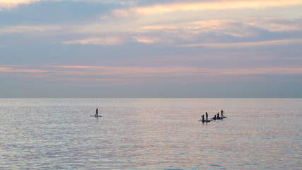 Fototapeta premium Team of young women standing up on a paddle surf board, enjoying a beautiful sunrise on the ocean