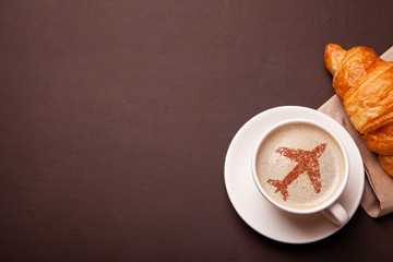 Cup of coffee with an airplane on the foam. Morning coffee with croissant in flight