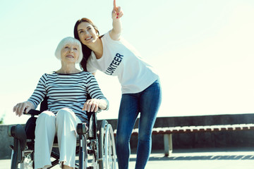 You see it. Pretty brunette keeping smile on her face and raising her left arm while pointing at sky