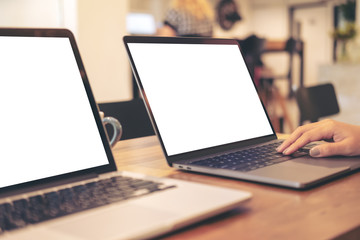 Mockup image of two laptop with blank white desktop screen on wooden table in office