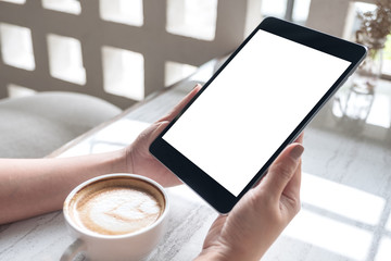 Mockup image of a woman holding black tablet pc with white blank screen with coffee cup on table