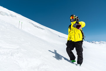 Fototapeta na wymiar Skier standing on a slope. Man in a light suit, the helmet and mask in skiing is to ski. In the background snow-capped mountains , skiers . Caucasus Mountains, Elbrus, Russia