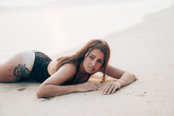 Portrait of a beautiful tender girl lies on the beach near the water, enjoys a sunbath rest, touched the face of sand, soft grains of sand stuck to her skin. Model with sand on his face posing lying