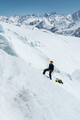 Fototapeta na wymiar A professional mountaineer in a helmet and ski mask on the insurance does notch the ice ax in the glacier. The work of a professional climber in winter on a glacier against the blue sky