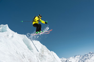 Fototapeta na wymiar A skier in full sports equipment jumps into the precipice from the top of the glacier against the background of the blue sky and the Caucasian snow-capped mountains. Elbrus region. Russia
