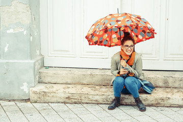 Young female sitting on stairs at the old city downtown.Raining day and autumn concept.