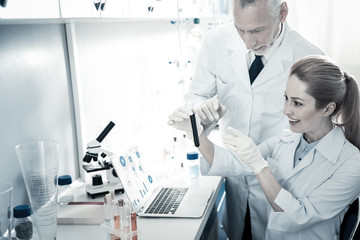 Successful research. Joyful smart nice biologists looking at the test sample and smiling while being happy about their successful research