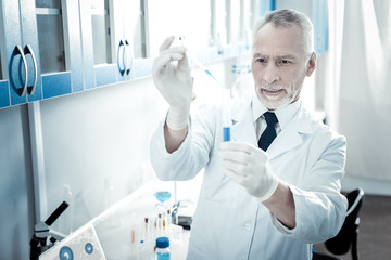 Biological engineering. Serious handsome male biologist standing in the lab and looking at the test tube while conducting a biological experiment