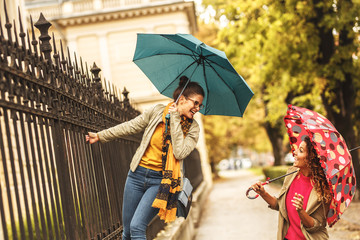Two female best friends making fun at the city street.Raining day and autumn concept.