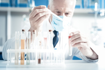 Laboratory analysis. Professional smart male biologist wearing protective mask and looking at the...