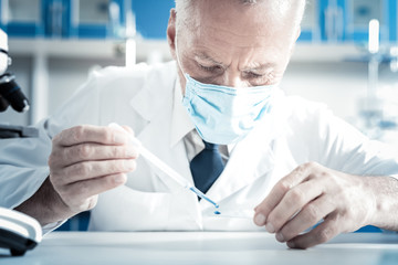 New discoveries. Smart experienced skillful biologist sitting at the table and looking at test...