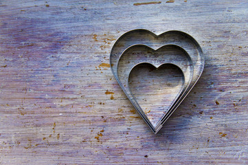 Three heart shaped metal cookie cutters, in a gungy vintage wood table surface.