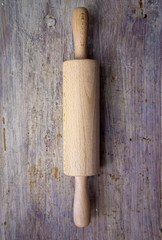 A wooden rolling pin on a worn wooden background.