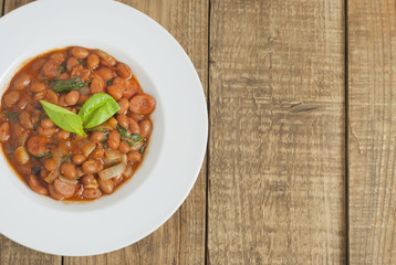 Cooked Red Beans in Tomato Sauce with Spinach and Onion, white Round Plate, Wooden Background, Top view, Copy space.