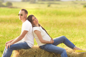 Naklejka na ściany i meble Young pregnant woman with her husband enjoying the nature wearing casual and style jeans and white t-shirt.