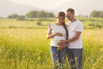 Young pregnant woman with her husband enjoying the nature wearing casual and style jeans and white t-shirt.