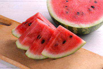 Bright ripe slices of watermelon on a cutting board with a big and juicy watermelon on a white wooden background