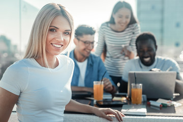 Fototapeta premium Lets work together. Cheerful girl sitting in semi position and leaning arm on the table while keeping smile on her face