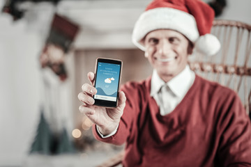 Weather checkup. Delighted old man expressing positivity while being at home and demonstrating his gadget