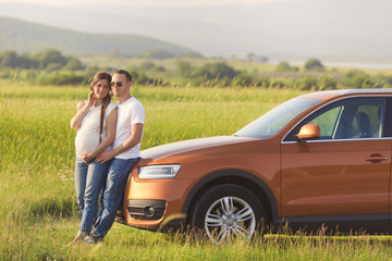 Young pregnant woman with her husband enjoying the nature. Traveling on family car in the field.