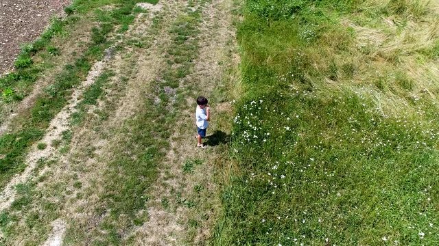 4K aerial footage of young boy walking and playing on fields in nature