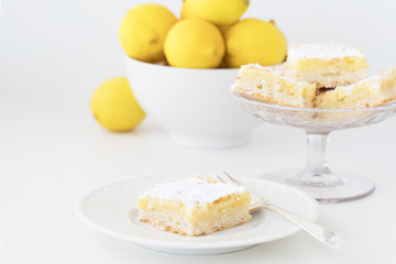 Photograph of Lemon Bars being served with lemons on white
