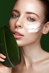 Beautiful fresh girl with cosmetic cream on the face, natural make-up and green leaves. Beauty face. Photo taken in the studio.